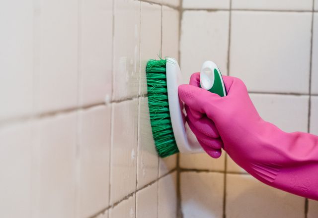 A gloved hand scrubbing bathroom tiles clean during a deep clean