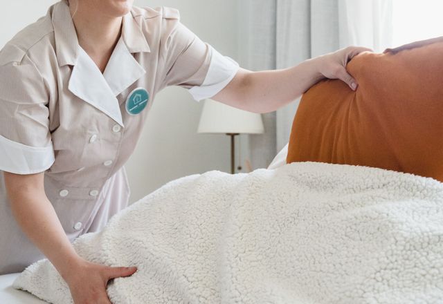 A housekeeper making a bed with fresh linen in a clean, sunlit bedroom