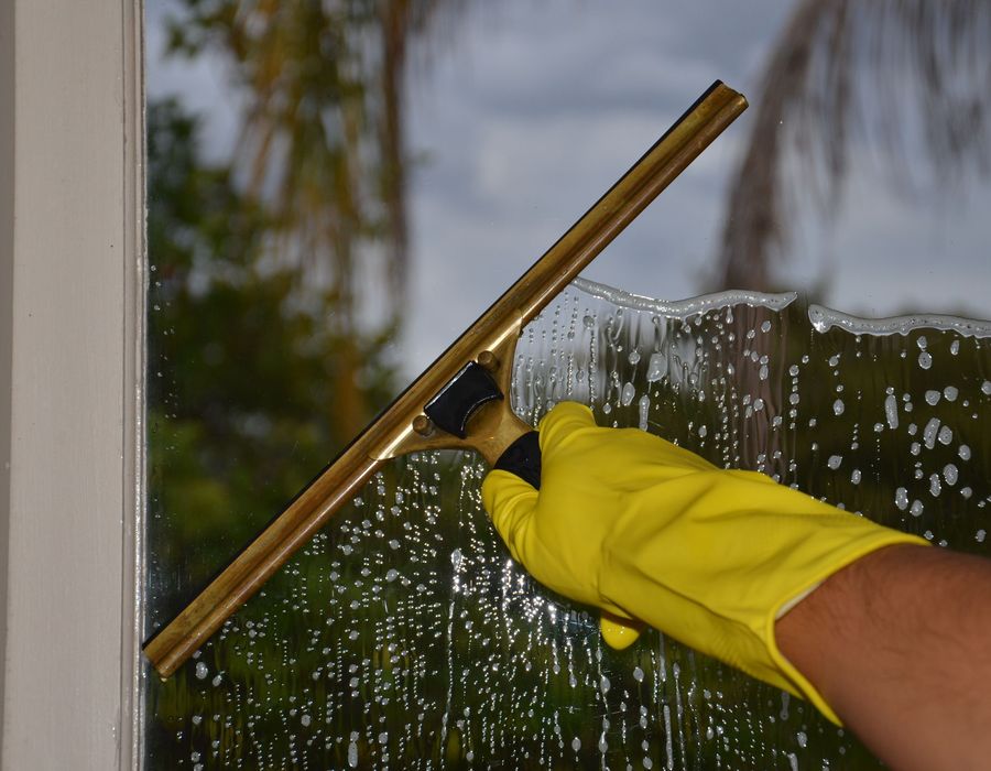 A professional cleaner pulling a squeegee across a large window, leaving it streak-free
